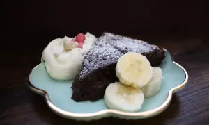 En bit nyttig kladdkaka med vispgrädde, bananskivor och strössel på en ljusblå tallrik.