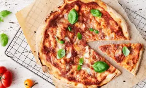 En nybakad pizza med tomatsås, ost och basilika. En bit är bortskuren. Tänk på kalorier pizza när du njuter!