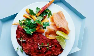 En tallrik med en röd omelett, rökt laxprotein, morotsstavar och limeklyftor.