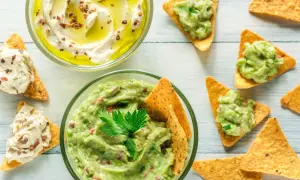 Två skålar med dipp, en med krämig hummus och en med färsk guacamole, serveras med tortillachips. Perfekt för en fiberrik matupplevelse.