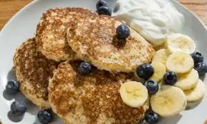 En tallrik med fluffiga bananpannkakor gjorda på havregryn, toppade med färska blåbär, bananskivor och en klick yoghurt. En perfekt frukost!