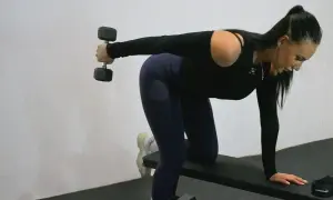 Kvinna tränar triceps med hantlar på en bänk.