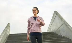 Glad kvinna i träningskläder går nerför en trappa. Ett bra sätt att gå ner i vikt med promenader.