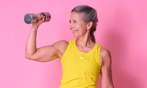 Glad kvinna med grått hår lyfter en 4 kg hantel, visar upp sina muskler. Hon inspirerar till frågan: hur mycket muskler kan man bygga på ett år?