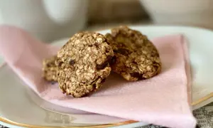 Tre hembakade, kalorisnåla kakor med havre och chokladbitar ligger på en ljusrosa servett på en vit tallrik.