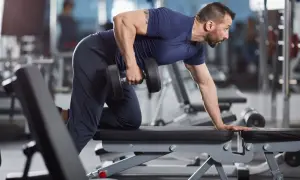 Man utför enarms hantelrodd på en träningsbänk i ett gym.