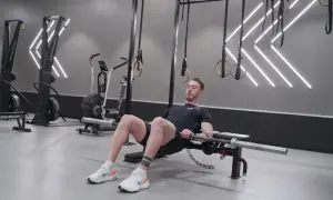 Man utför hip thrust med skivstång på en bänk i ett modernt gym.
