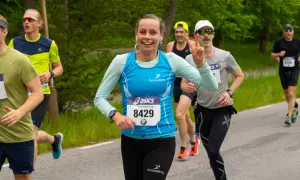 Glada löpare kämpar på en mil. En kvinna med nummer 8429 ler och gör segertecken.