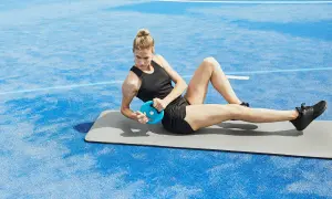 Kvinna gör sneda sit-ups med en blå viktplatta på en matta utomhus.
