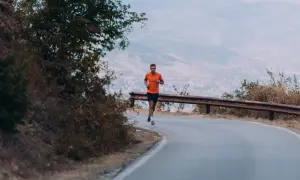 Man i orange tröja springer på en kurvig väg, fokuserad på att bygga upp kondition i vacker natur.