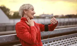 Glad kvinna kollar sin puls på handleden, 130 i puls vid promenad. Solnedgång i bakgrunden.