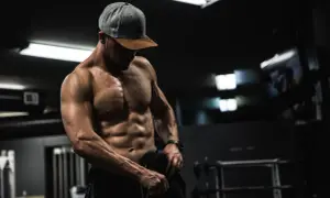 Muskulös man i gym, visar upp sina magrutor. Frågan "hur får man magrutor" besvaras med dedikation och träning.