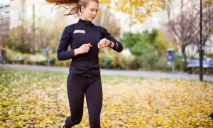 Kvinna springer i parken bland höstlöv och kollar sin klocka, hoppas på en bra tid på 5 km.