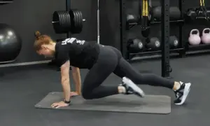 Kvinna gör mountain climbers på en träningsmatta i ett gym. Hon verkar ha dålig kondition, men kämpar på.