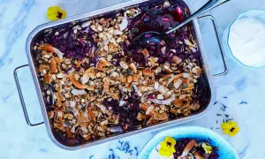 En härlig, nyttig dessert med bär och granola i en ugnsform. Serveras med en klick yoghurt och garnerad med blommor.