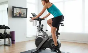 Kvinna tränar på motionscykel, följer instruktioner på skärmen. Kondition fakta för en hälsosam livsstil.