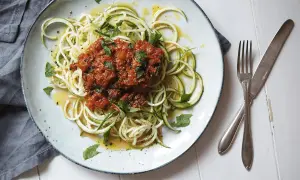 En tallrik med zucchini-spaghetti och köttfärssås, ett av många zucchini nyttiga recept. Garnerad med färska örter och en gnutta citronzest.