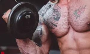 Muskulös man med tatueringar lyfter en 30 kg hantel. En del av resan för att gå ner i vikt och bygga muskler.