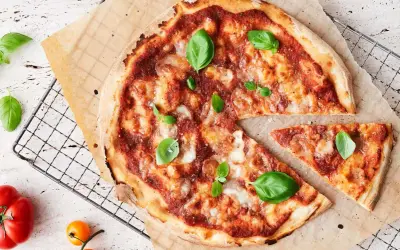 En nybakad pizza med tomatsås, ost och basilika. En bit är bortskuren. Tänk på kalorier pizza när du njuter!