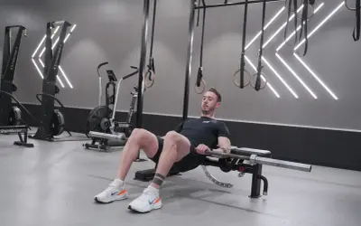 Man utför hip thrust med skivstång på en bänk i ett modernt gym.