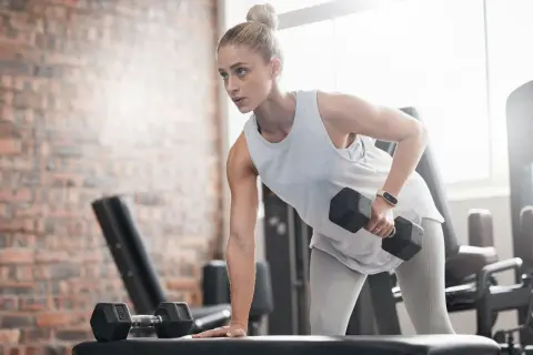 Kvinna tränar med hantlar på gym, fokuserad på att gå ner i vikt.