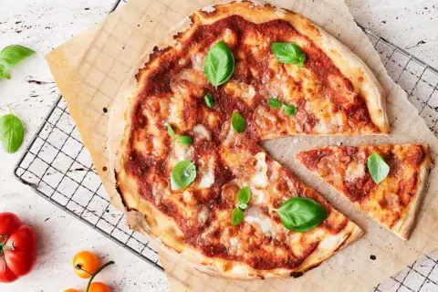 En nybakad pizza med tomatsås, ost och basilika. En bit är bortskuren. Tänk på kalorier pizza när du njuter!