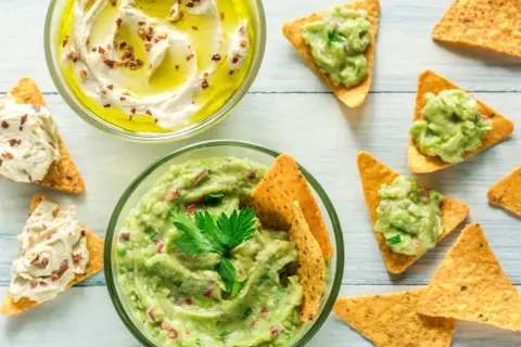 Två skålar med dipp, en med krämig hummus och en med färsk guacamole, serveras med tortillachips. Perfekt för en fiberrik matupplevelse.