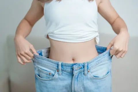 En person visar upp sina för stora jeans, ett tecken på att hon lyckats med hur man går ner i vikt.