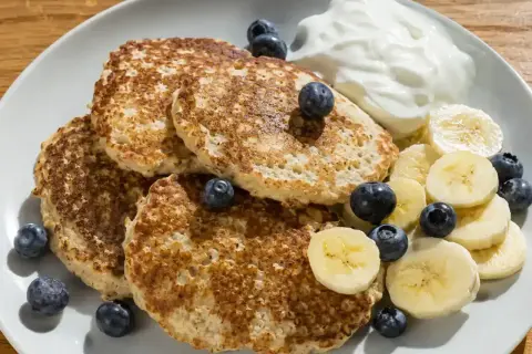 En tallrik med fluffiga bananpannkakor gjorda på havregryn, toppade med färska blåbär, bananskivor och en klick yoghurt. En perfekt frukost!