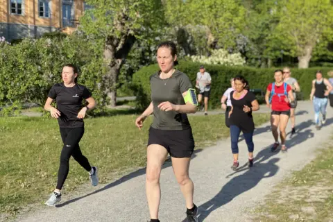 En grupp löpare, mestadels kvinnor, tar sig fram på en grusväg i en park. De är på väg att springa en mil i det vackra vårvädret.