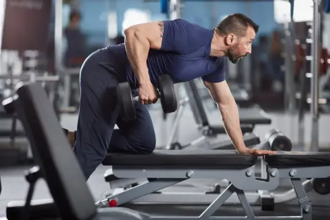 Man utför enarms hantelrodd på en träningsbänk i ett gym.