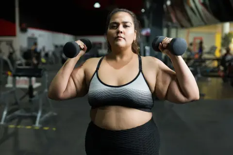 En kvinna lyfter hantlar på gymmet, en del av hennes träningsresa för att gå ner i vikt.