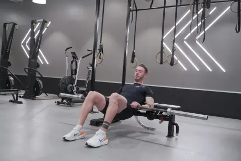 Man utför hip thrust med skivstång på en bänk i ett modernt gym.