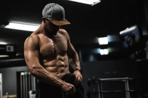 Muskulös man i gym, visar upp sina magrutor. Frågan "hur får man magrutor" besvaras med dedikation och träning.