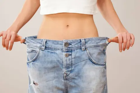 En person visar upp sina för stora jeans, ett tydligt tecken på att de lyckats gå ner i vikt.