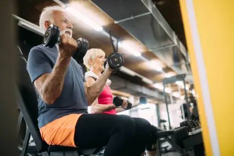 Äldre par tränar med hantlar på gym. De visar att sarkopeni betyder minskad muskelmassa, men att träning kan motverka detta.