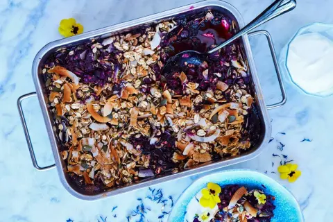 En härlig, nyttig dessert med bär och granola i en ugnsform. Serveras med en klick yoghurt och garnerad med blommor.