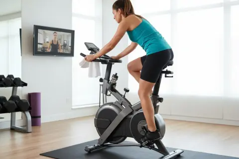 Kvinna tränar på motionscykel, följer instruktioner på skärmen. Kondition fakta för en hälsosam livsstil.