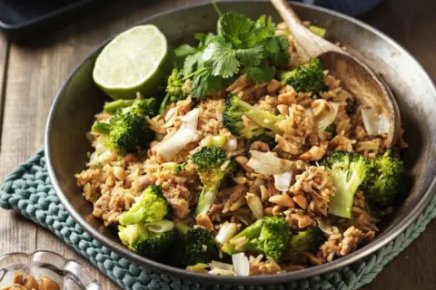 En skål med stekt ris med broccoli, jordnötter och en limeklyfta. En perfekt nyttig lunch.
