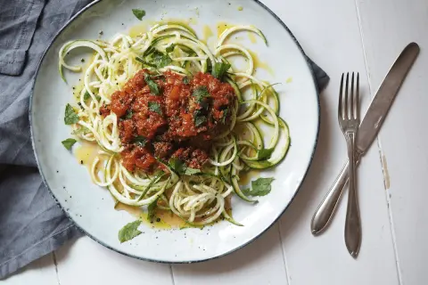 En tallrik med zucchini-spaghetti och köttfärssås, ett av många zucchini nyttiga recept. Garnerad med färska örter och en gnutta citronzest.