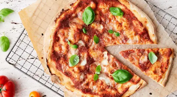 En nybakad pizza med tomatsås, ost och basilika. En bit är bortskuren. Tänk på kalorier pizza när du njuter!