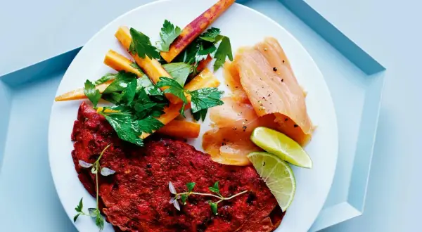 En tallrik med en röd omelett, rökt laxprotein, morotsstavar och limeklyftor.