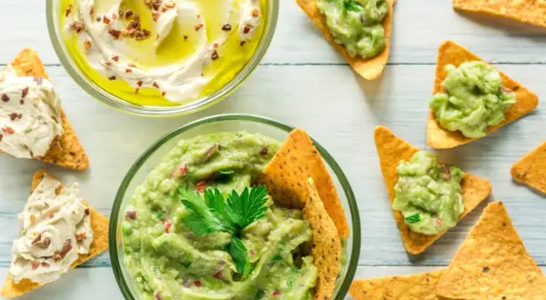 Två skålar med dipp, en med krämig hummus och en med färsk guacamole, serveras med tortillachips. Perfekt för en fiberrik matupplevelse.