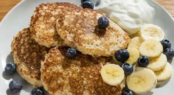 En tallrik med fluffiga bananpannkakor gjorda på havregryn, toppade med färska blåbär, bananskivor och en klick yoghurt. En perfekt frukost!