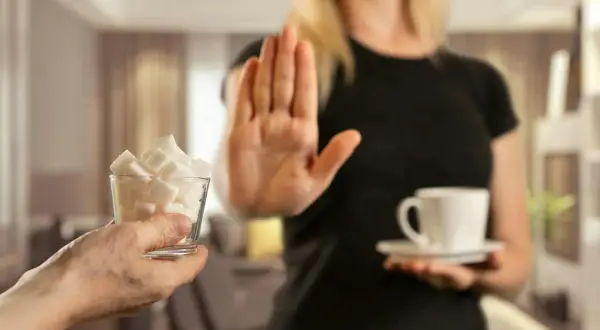 En person nekar sockerbitar och en kopp kaffe, en symbol för att sluta med socker och undvika biverkningar.