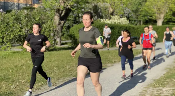 En grupp löpare, mestadels kvinnor, tar sig fram på en grusväg i en park. De är på väg att springa en mil i det vackra vårvädret.