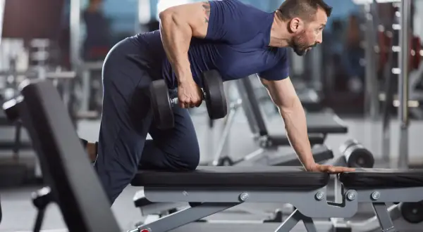 Man utför enarms hantelrodd på en träningsbänk i ett gym.