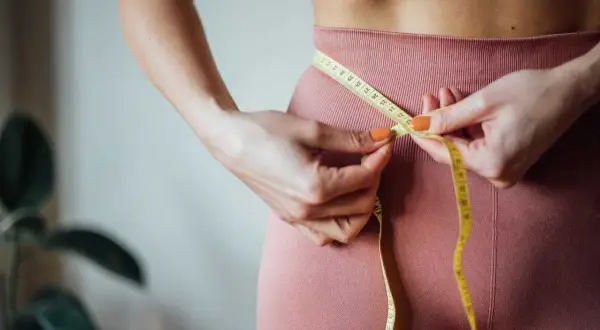 En person mäter midjan med ett måttband. Frågan "hur mycket kan man gå ner i vikt med Ozempic?" dyker upp när man ser resultaten av en hälsosam livsstil.