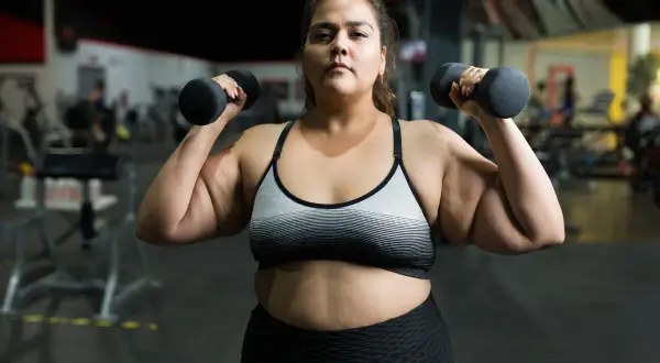 En kvinna lyfter hantlar på gymmet, en del av hennes träningsresa för att gå ner i vikt.