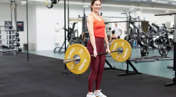 Kvinna i gym utför marklyft med skivstång. Träning för marklyft muskler.
